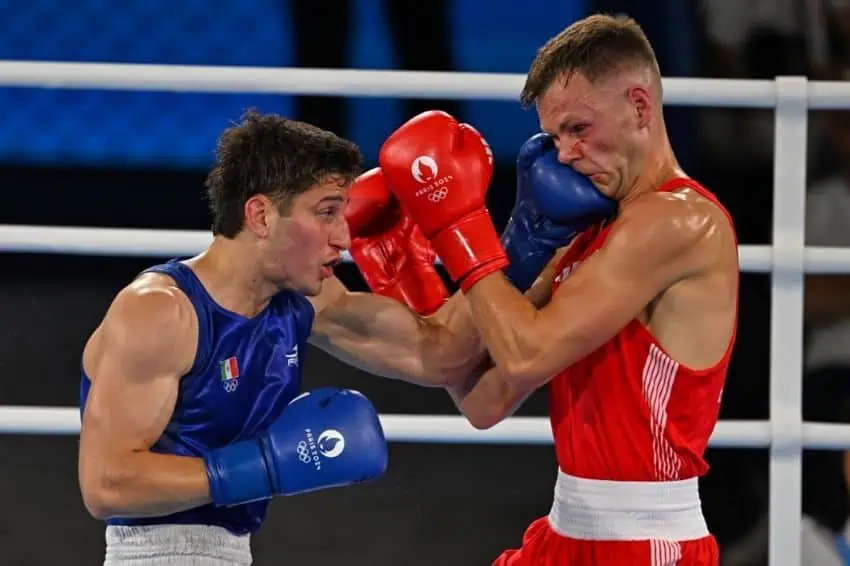 Dos hombres boxear en un anillo de boxeo blanco. Uno lleva guantes rojos y el otro azul. Ambos guantes tienen el logotipo de los Juegos Olímpicos de París. El boxeador en azul es Marco Verde de México y el de Red es Lewis Richardson del Reino Unido