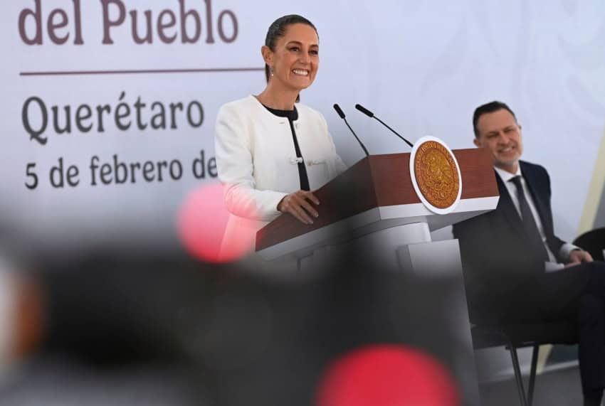 President Claudia Sheinbaum smiling as she stands behind the presidential podium at her daily press conference. She