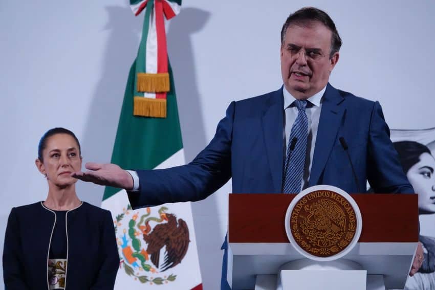 Economy Minister Marcelo Ebrard gestures while standing at a podium as President Claudia Sheinbaum looks on
