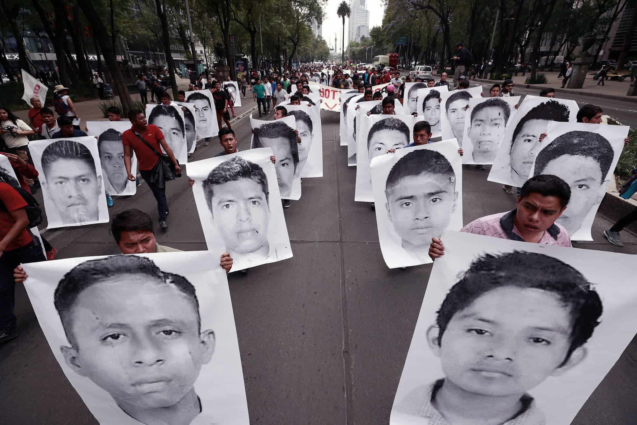 Protesters holding up posters the size of their bodies that show different members of the so-called Ayotzinapa 43 students as they march down a Mexico City street.