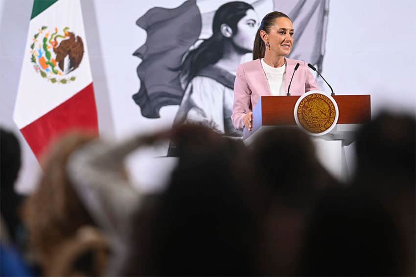 Sheinbaum stands smiling at a podium