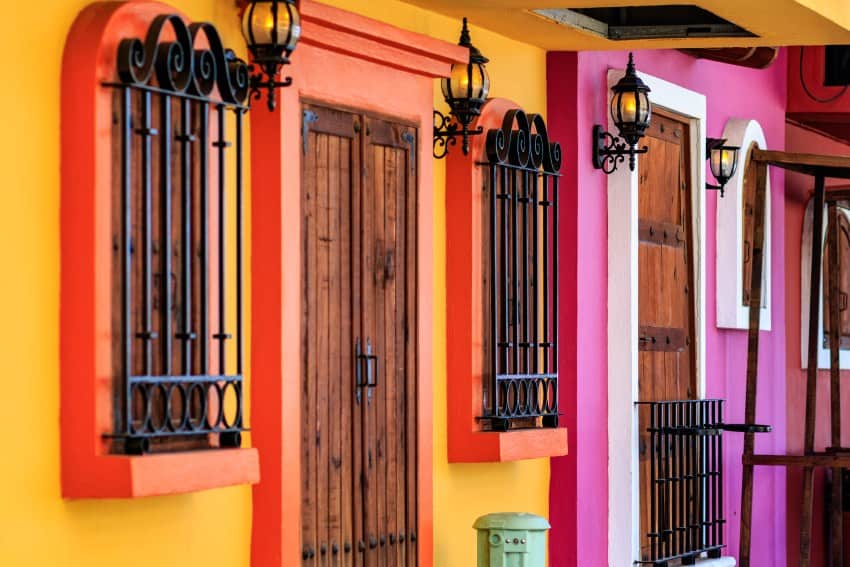 Facades de la casa en una calle pintada en diferentes colores brillantes y alegres con pintorescas rejillas de hierro forjado negros sobre muchas puertas y ventanas y lámparas retro hechas para parecer lámparas de gas.