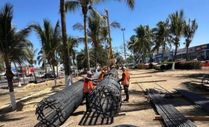 Trabajadores de la construcción desactivando grandes tubos de cable en una larga área de tierra rodeada de palmeras en Puerto Vallarta