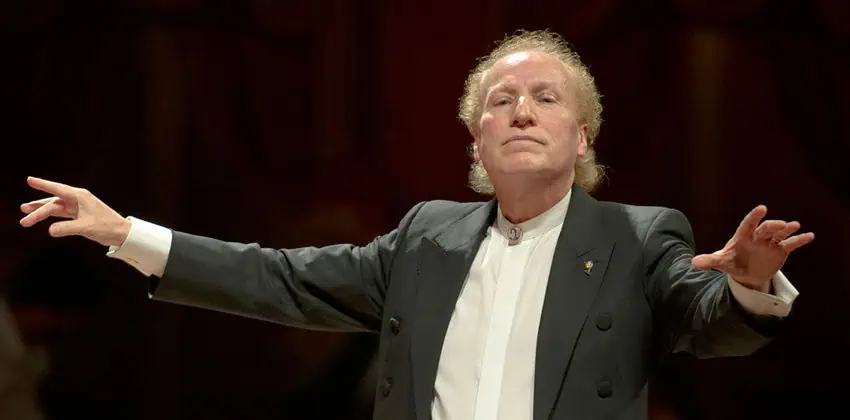 El director mexicano Arturo Diemecke atrapado en la dirección media. Lleva una chaqueta de esmoquin y una camisa blanca en el cuello con un broche.