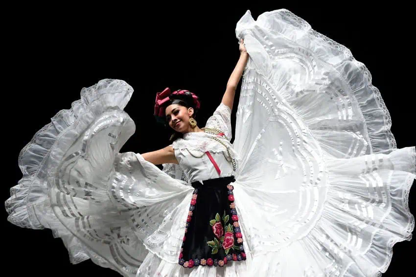 Una joven mujer mexicana con un vestido de baile folklórico mexicano tradicional con una enorme enagua que está sosteniendo a cada lado como parte de un movimiento de baile.