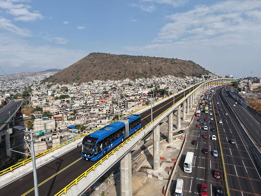 Un trolleybus azul corre en una pista elevada sobre una carretera con la Ciudad de México urbano en el fondo