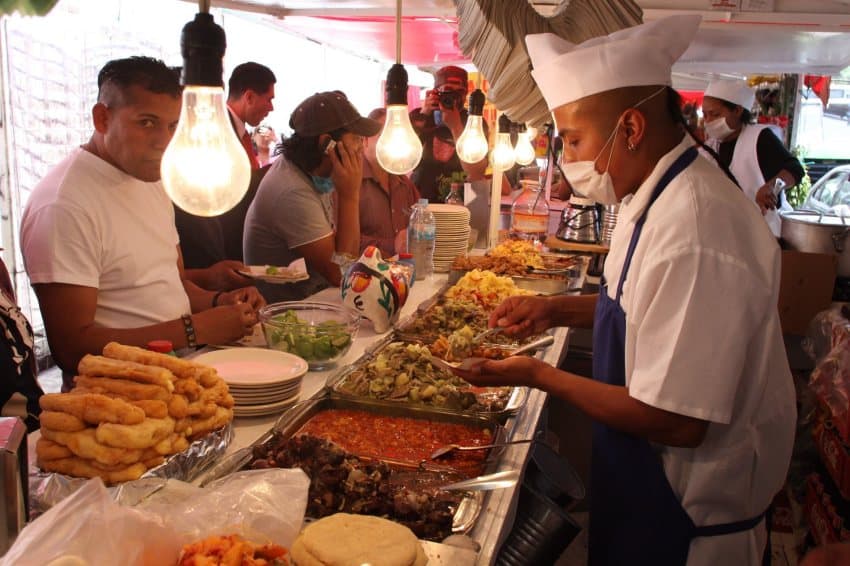 Los residentes de la Ciudad de México de pie y sentados en un puesto de taco temporal mientras esperaban que los empleados llenen sus tacos con artículos cocinados en bandejas buffet.