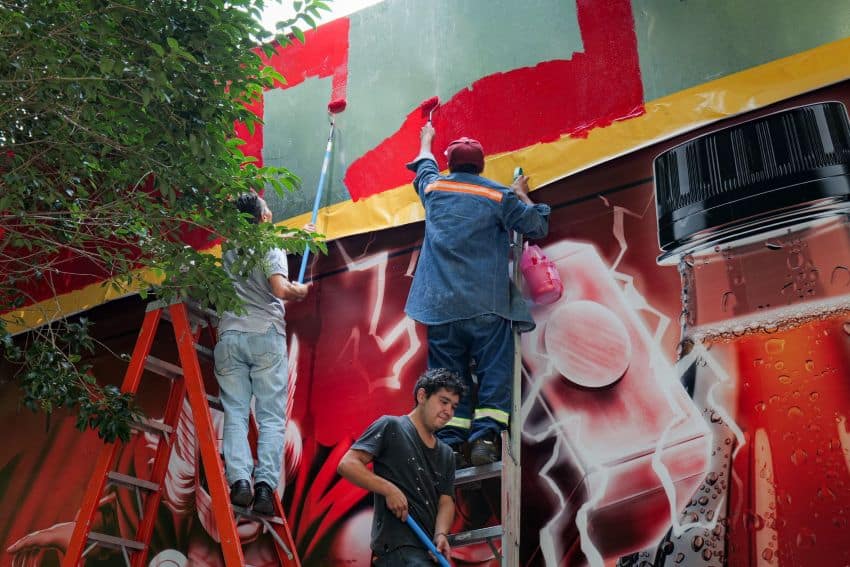 Los trabajadores con rodillos de pintura que crean un anuncio para Coca-Cola en un vecindario de la Ciudad de México.