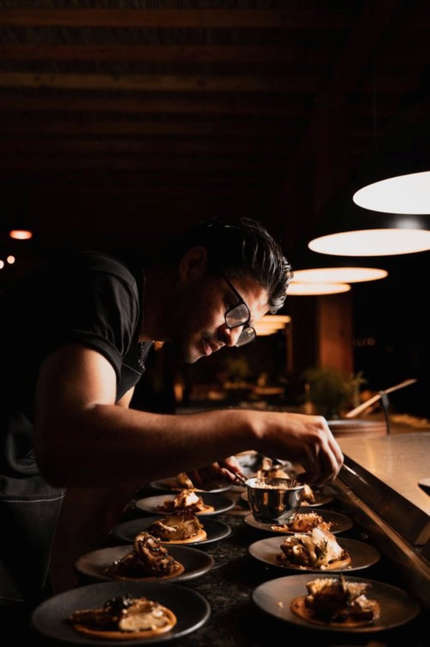 Un chef de línea que adorna pequeños platos de comida de restaurantes en una zona de escenario de la cocina del restaurante.