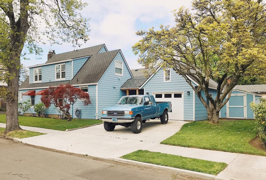 Una camioneta frente a una casa pintada azul en un suburbio estereotípico de los Estados Unidos