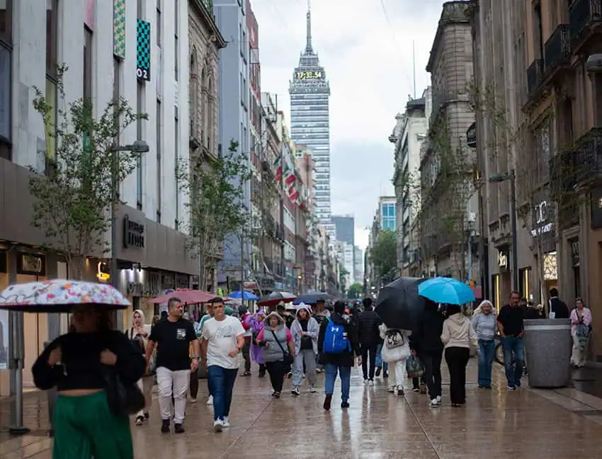 La gente camina por la Ciudad de México con paraguas, con la Torre de América Latina en el fondo