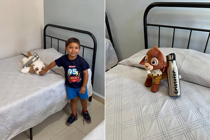 Un niño se para al lado de una cama con una botella de agua y un juguete