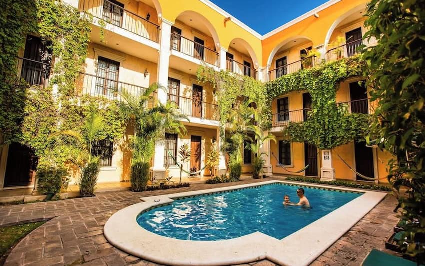 Un hotel colonial con paredes amarillas y arcos blancos. Una piscina está en primer plano.