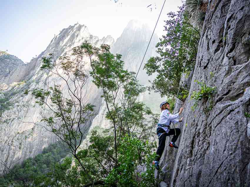 Un escalador de roca asciende una pared de piedra caliza en El Potrero Chico, México, con picos dramáticos en el fondo.