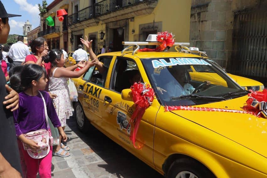 Los peatones dienden al taxi decorado en Oaxaca, el taxista arroja regalos desde la ventana