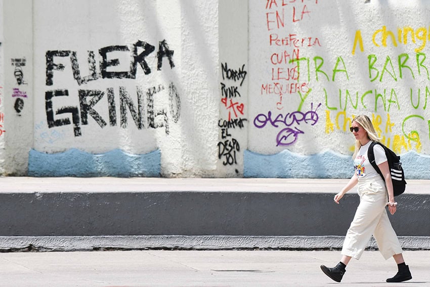 A blonde woman walks past graffiti reading