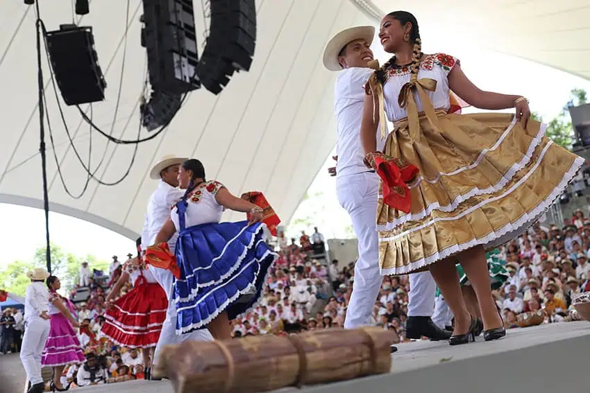 Dancers in traditional garb including long colorful skirts dance on a stage a Guelaguetza in Oaxaca