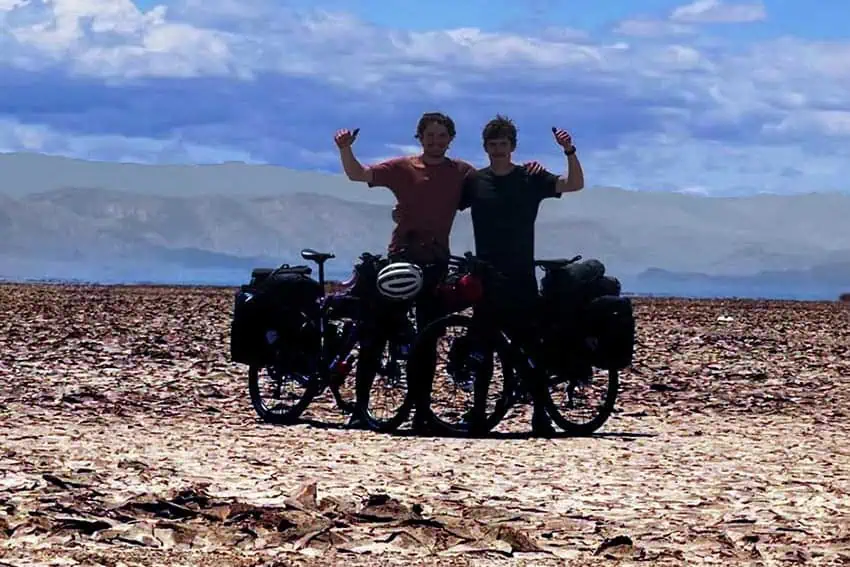 Dos ciclistas con los brazos levantados en el aire posando en el desierto