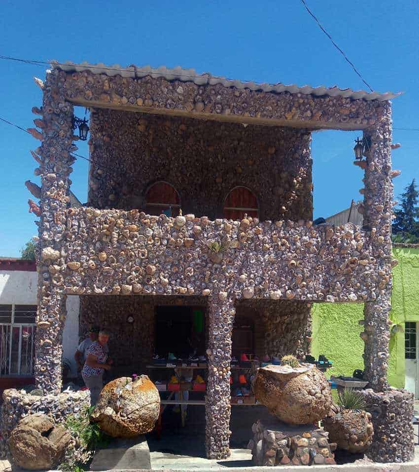 Un edificio único de dos pisos en la ciudad de Asientos, Aguascalientes, México. Todo el exterior está cubierto de pequeñas piedras. El edificio tiene un pequeño balcón y grandes rocas redondas en el frente, con cosas a la venta en el piso inferior, que está al aire libre.