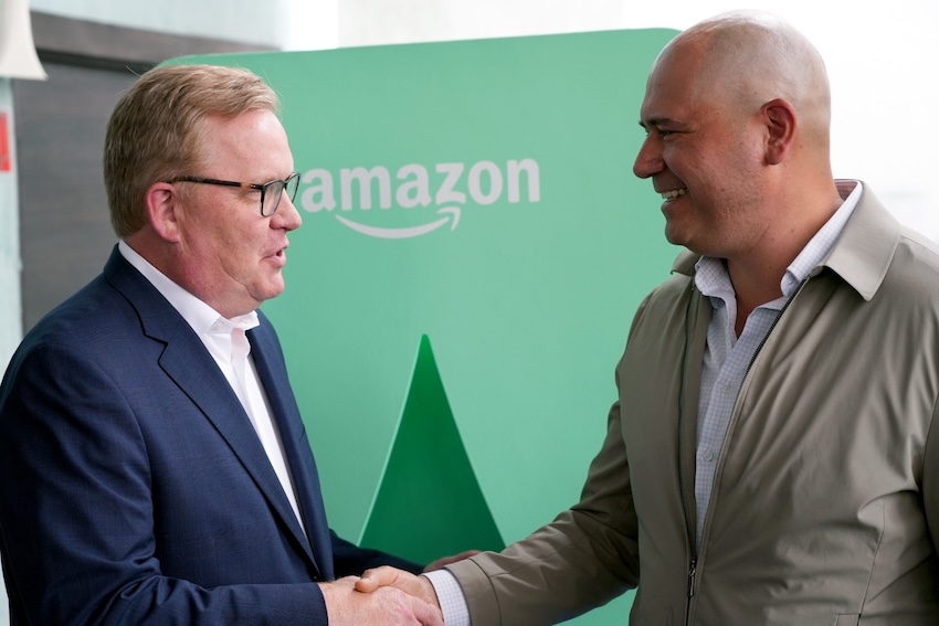 Two men shake hands in front of an Amazon logo in Mexico City