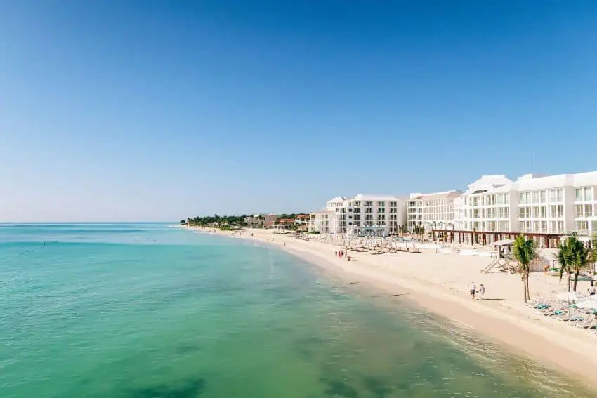 Una playa de arena blanca con agua turquesa y torres de condominios en la Riviera Maya