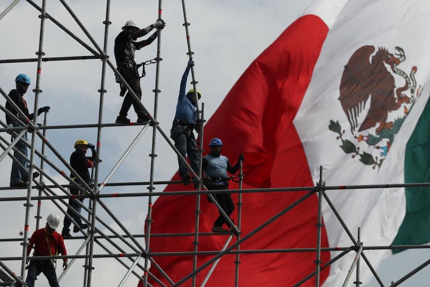 workers on scaffolding in front of a Mexican flag