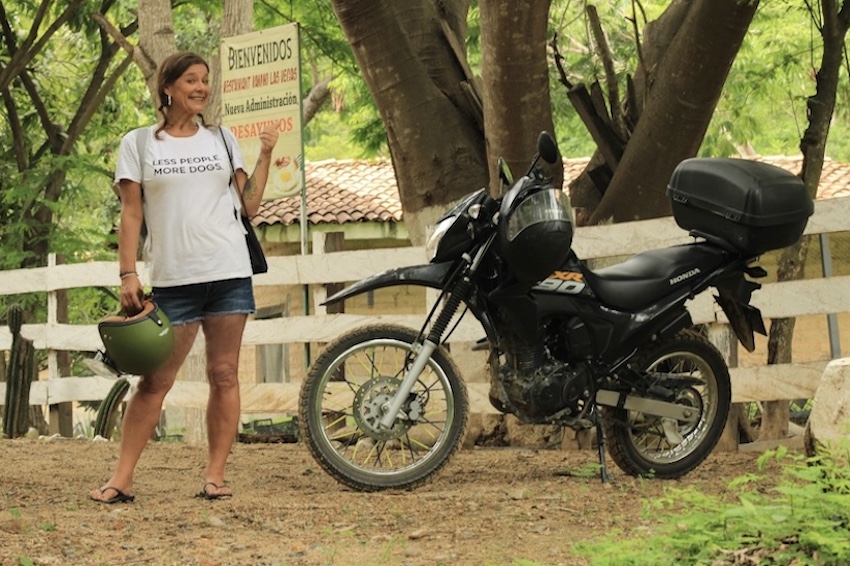 A woman in a white t-shirt stands next to a black touring motorcycle