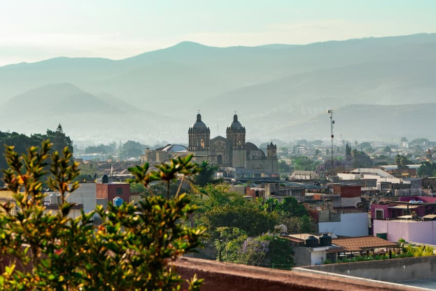 Una vista panorámica del paisaje urbano histórico de la ciudad de Oaxaca, México. La ciudad se ve enclavada en un valle rodeado de montañas brumosas.