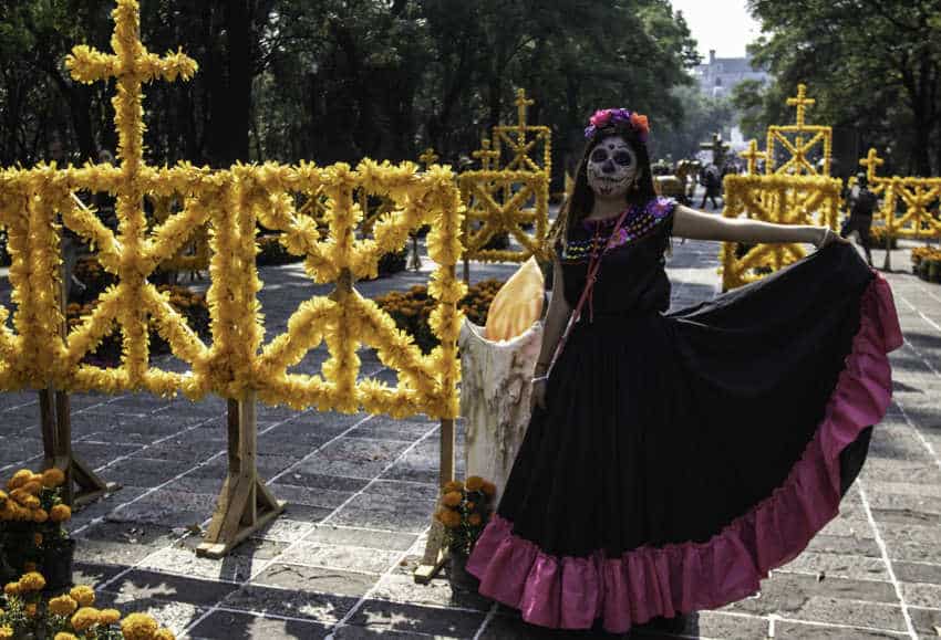 Mujer con un traje tradicional mexicano con una corona de flores y el rostro pintado de blanco como una Catrina, típico de las festividades del Día de Muertos en la Ciudad de México en noviembre.