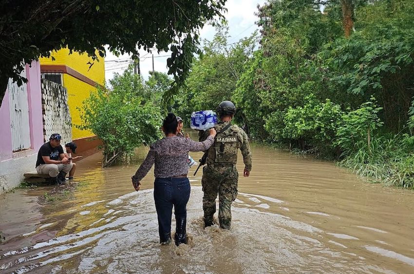Una mujer camina con un miembro de la Marina a través del agua hasta las rodillas después de fuertes lluvias en el centro de México