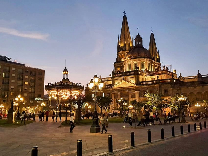 People walk by a Guadalajara cathedral lit up in the evening