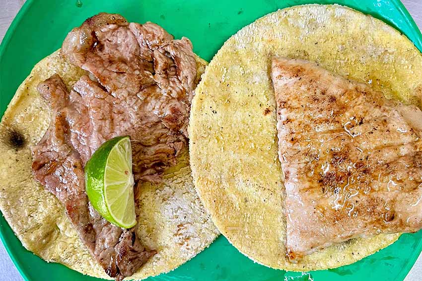 Dos tortillas con carne encima, presentadas en un plato verde y con una rodaja de limón