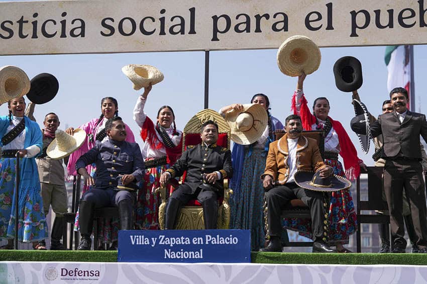 Personas vestidas con trajes históricos viajan en una carroza con la etiqueta Villa y Zapata 