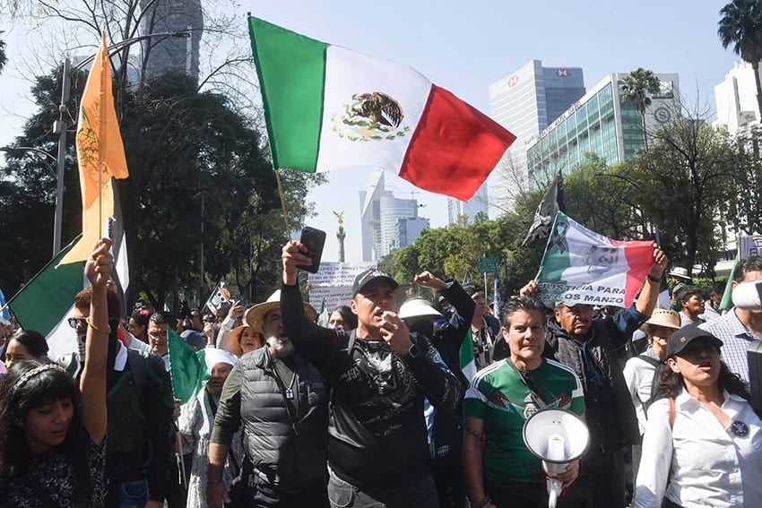 Mexicanos de mediana edad marchan por el Paseo de la Reforma con banderas mexicanas