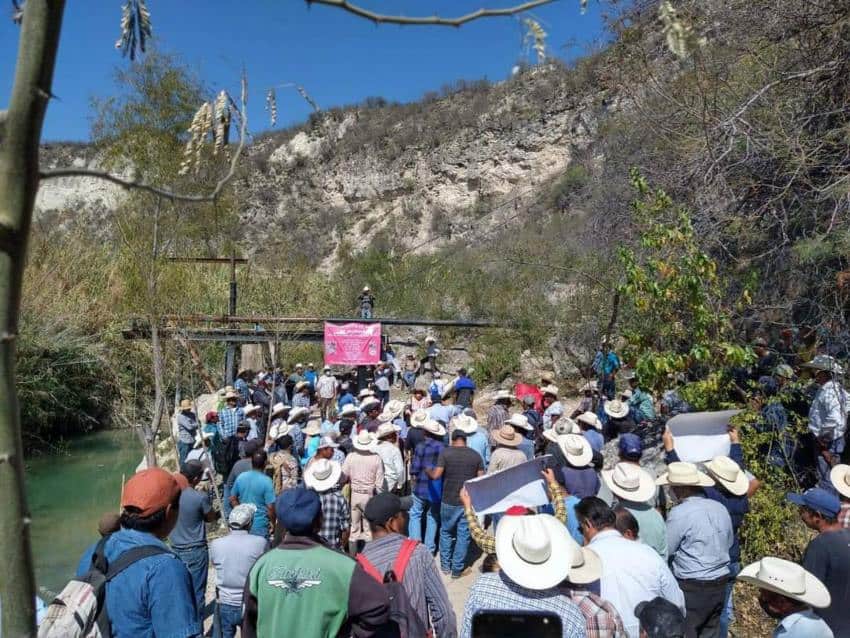 Hombres mexicanos con camisetas y camisas con botones, muchos de ellos con sombreros de vaquero, se reunieron en una multitud en un puente sobre un pequeño río en Jamauve, Tamaulipas.
