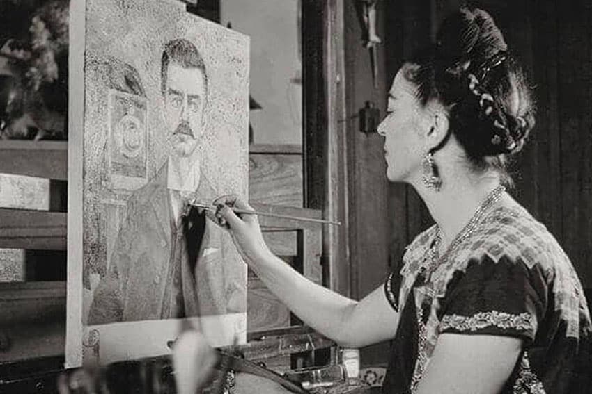Fotografía en blanco y negro de Frida Kahlo mirando un cuadro en el que está trabajando de un retrato de su padre, Guillermo Kahlo.