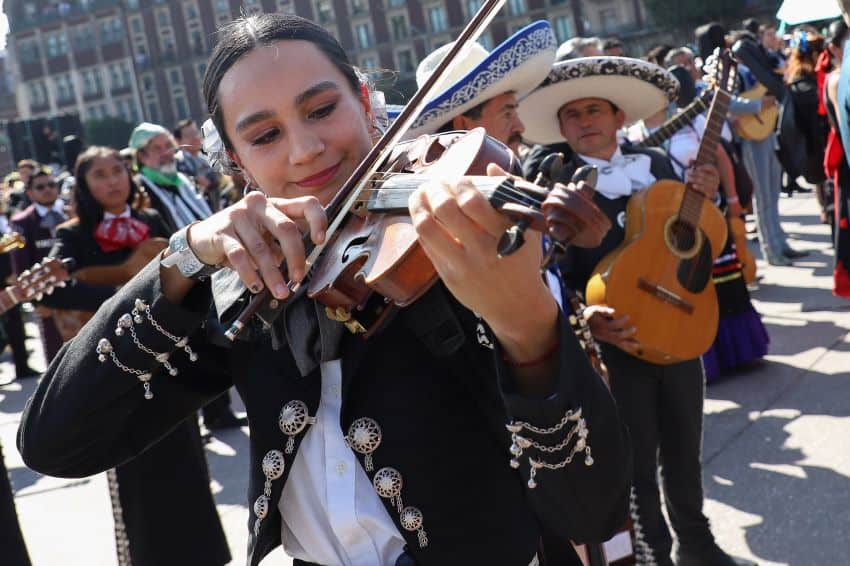 Una mujer vestida de mariachi toca el violín, rodeada de otros músicos de mariachi mientras intentan romper el récord mundial Guinness de mayor actuación.