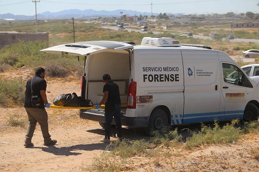 Hombres con uniformes oscuros cargan bultos negros en una furgoneta con la etiqueta "Servicio médico forense"