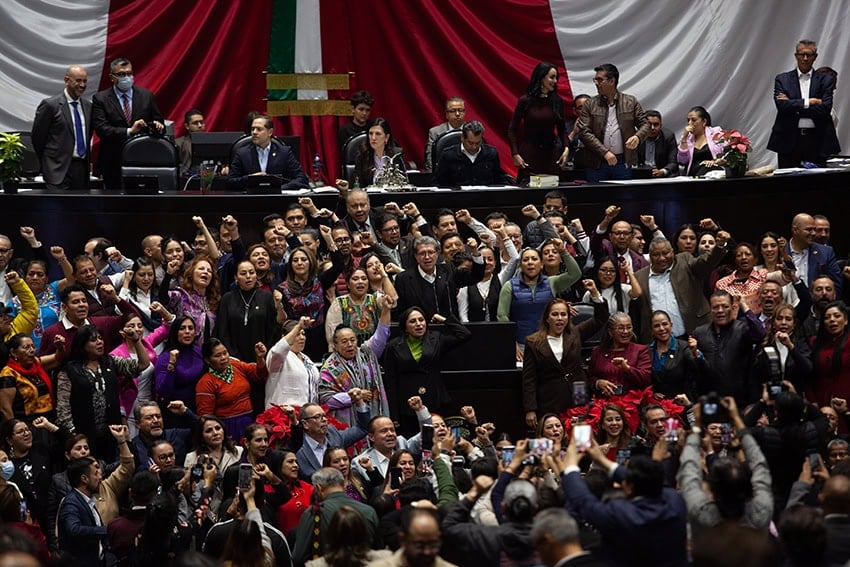 Ricardo Monreal se encuentra en un podio de la Cámara de Diputados de México (cámaras del congreso) rodeado por decenas de simpatizantes con los puños en alto.