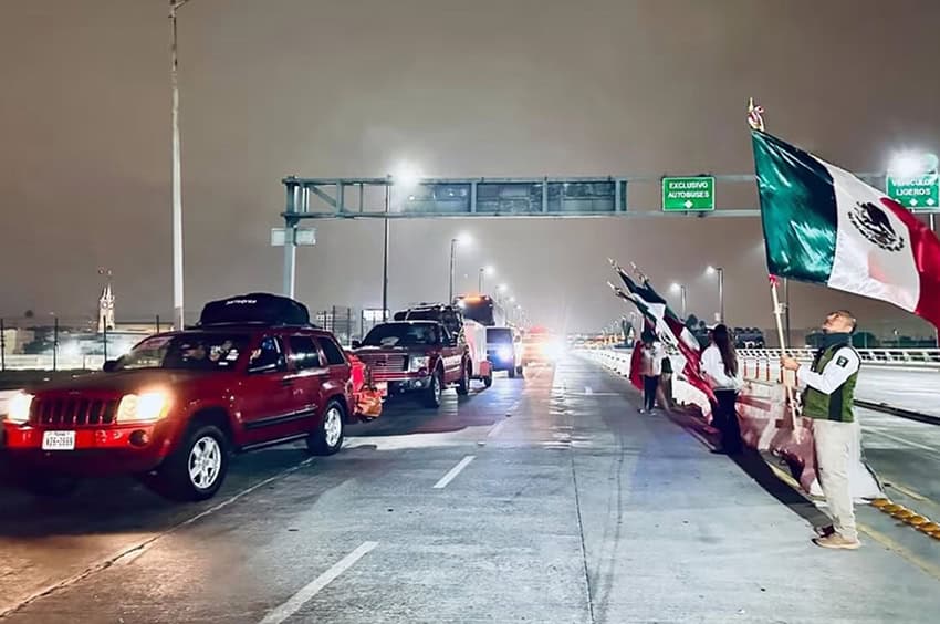Government agents wave Mexican flags as a caravan of cars drives down a highway at night
