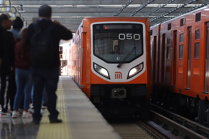 Riders wait as an orange Mexico City Metro train pulls into the station
