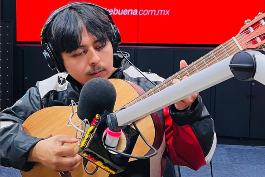 Joven mexicano tocando una guitarra acústica con un micrófono de radio en un programa de prensa en México