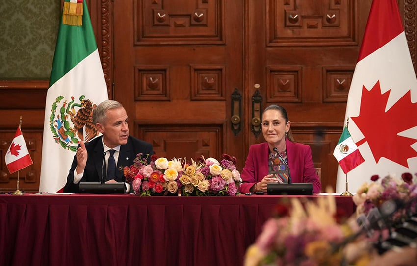 El presidente Sheinbaum y el primer ministro de Canadá, Mark Carney, se sientan en una mesa en el Palacio Nacional con banderas de Canadá y México.