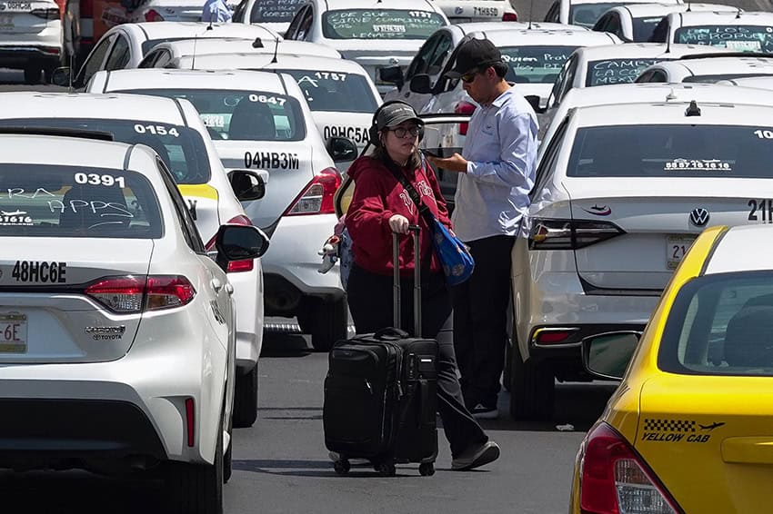 Los pasajeros del aeropuerto que remolcan el equipaje se entrelazan entre los taxis que bloquean una carretera cerca del aeropuerto.