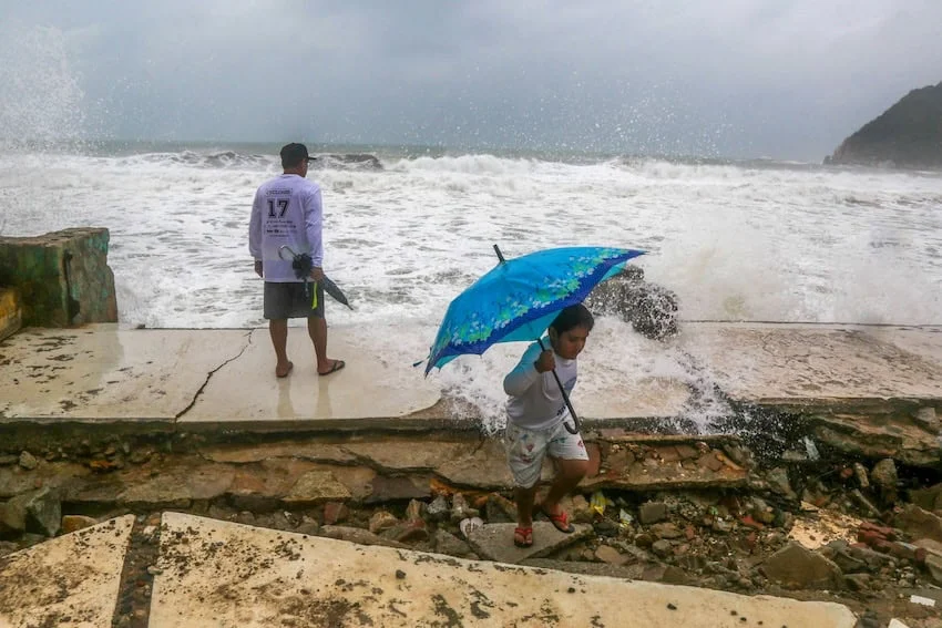 Dos personas se agachan para evitar las salpicaduras de agua del océano mientras un huracán se acerca a México