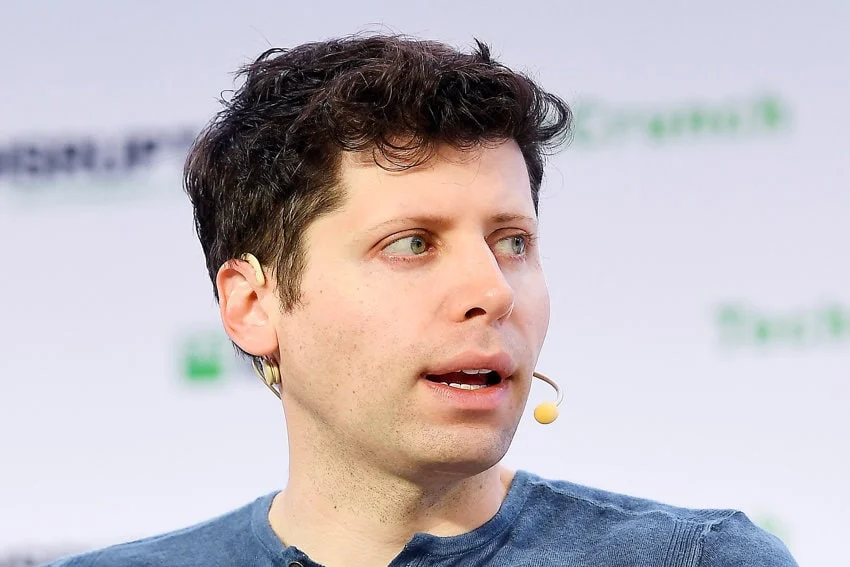 Una fotografía de primer plano de Sam Altman, director de la empresa de tecnología de inteligencia artificial OpenAI. Lleva un pequeño micrófono montado en la oreja y habla en un evento público.